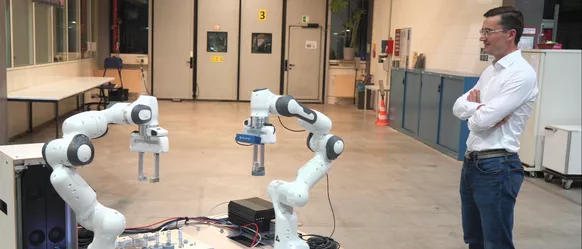 Wissenschaftler Jonas Wittmann beobachtet seine zwei KI-gesteuerten Roboterarme. 